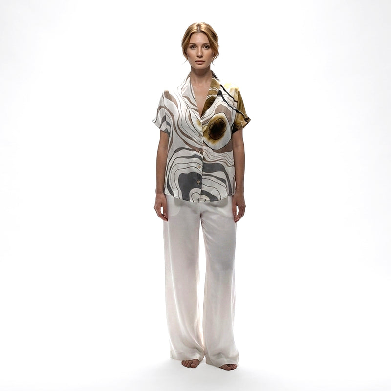 Front view of the abstract brown, grey and gold print shirt styled with white wide-leg trousers