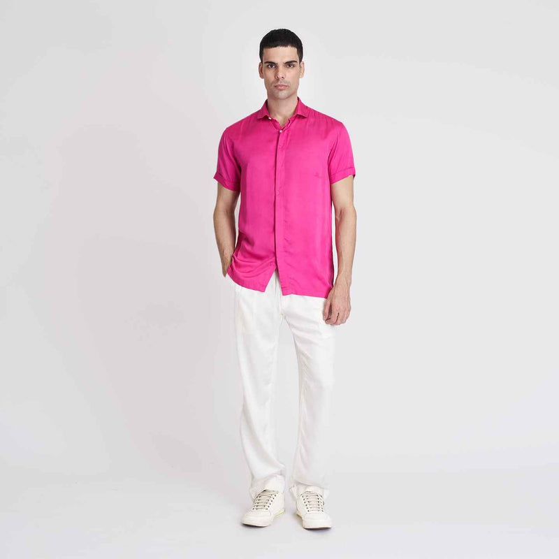 Front view of the solid hot pink camp shirt, full length with white trousers