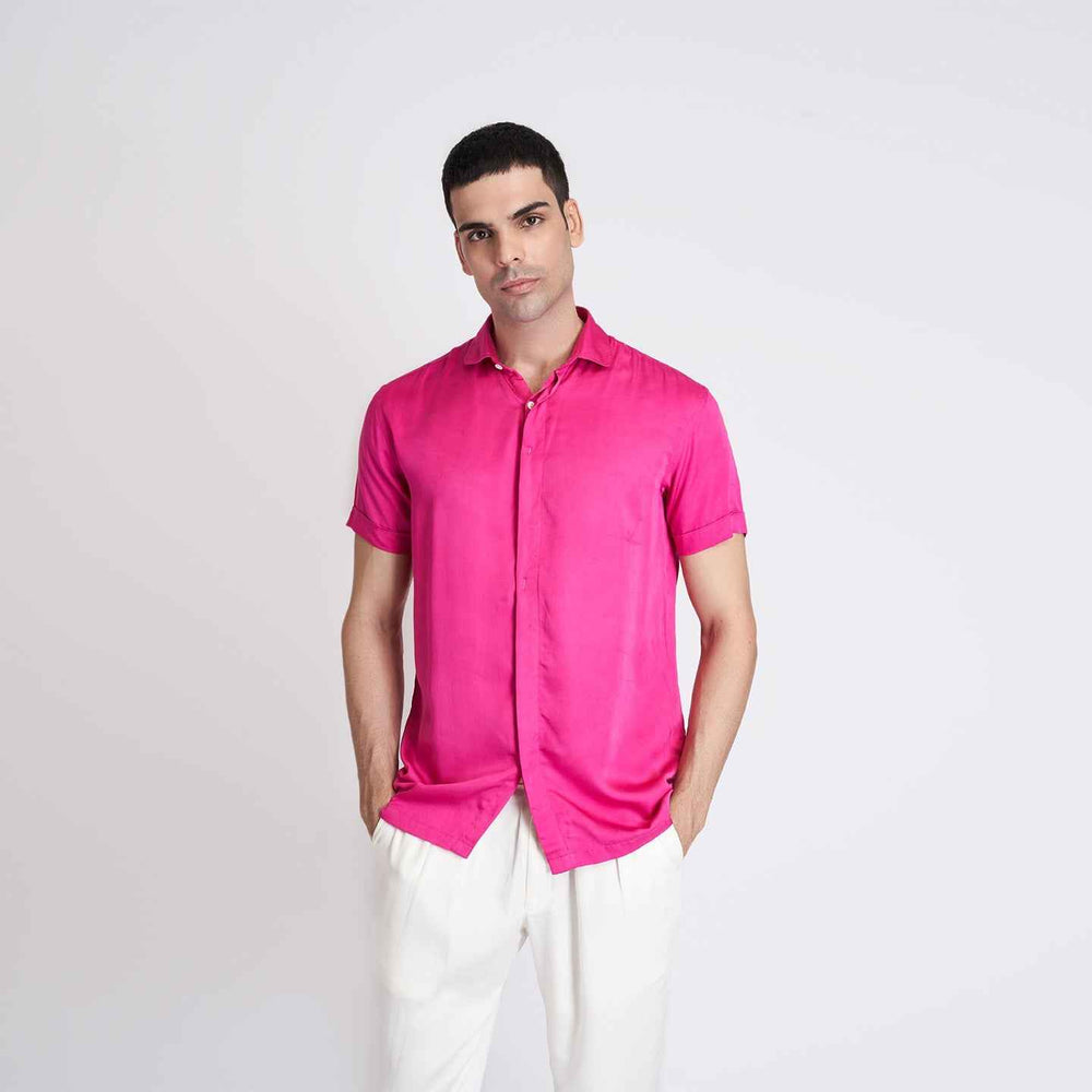 Front view of the solid hot pink short-sleeve camp shirt styled with white trousers
