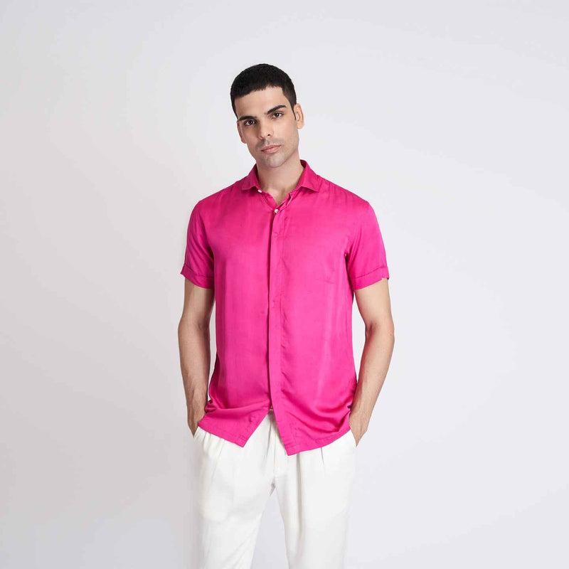 Front view of the solid hot pink short-sleeve camp shirt styled with white trousers