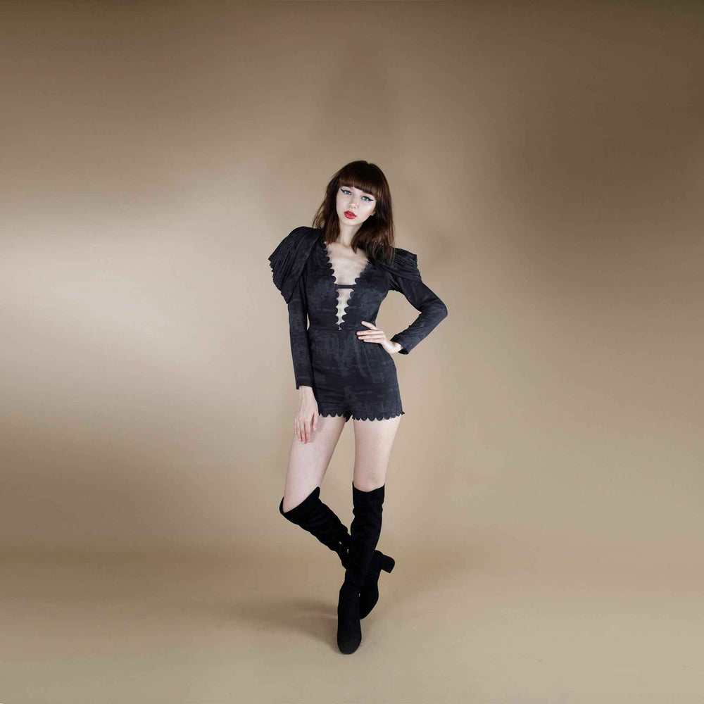 Front view of the black plunge-neck jumpsuit with puff sleeve and scalloped trim, styled with over-the-knee boots