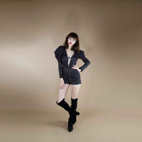 Front view of the black plunge-neck jumpsuit with puff sleeve and scalloped trim, styled with over-the-knee boots