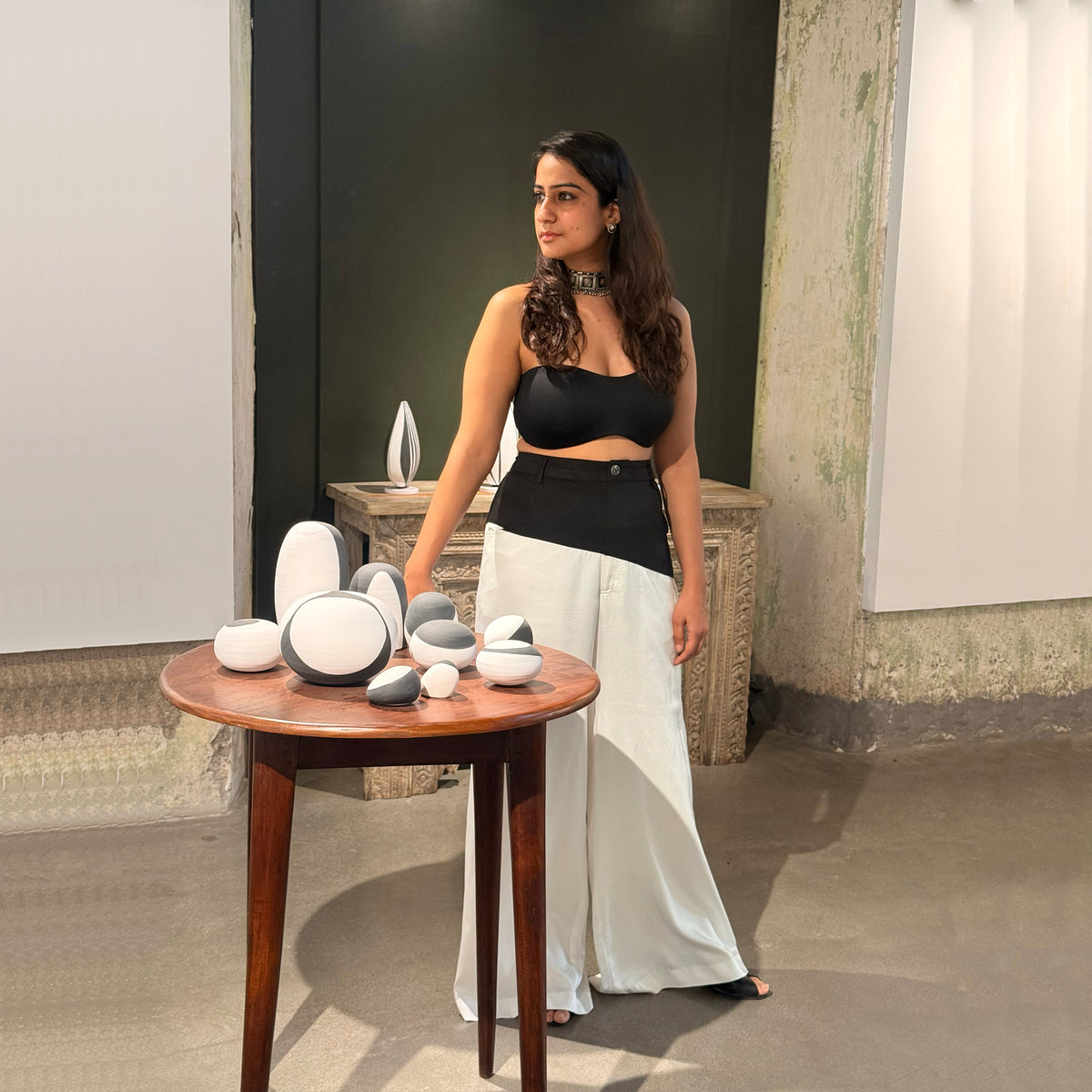 Close-up front view of the white wide-leg Gemini pants and black crop top in a gallery setting
