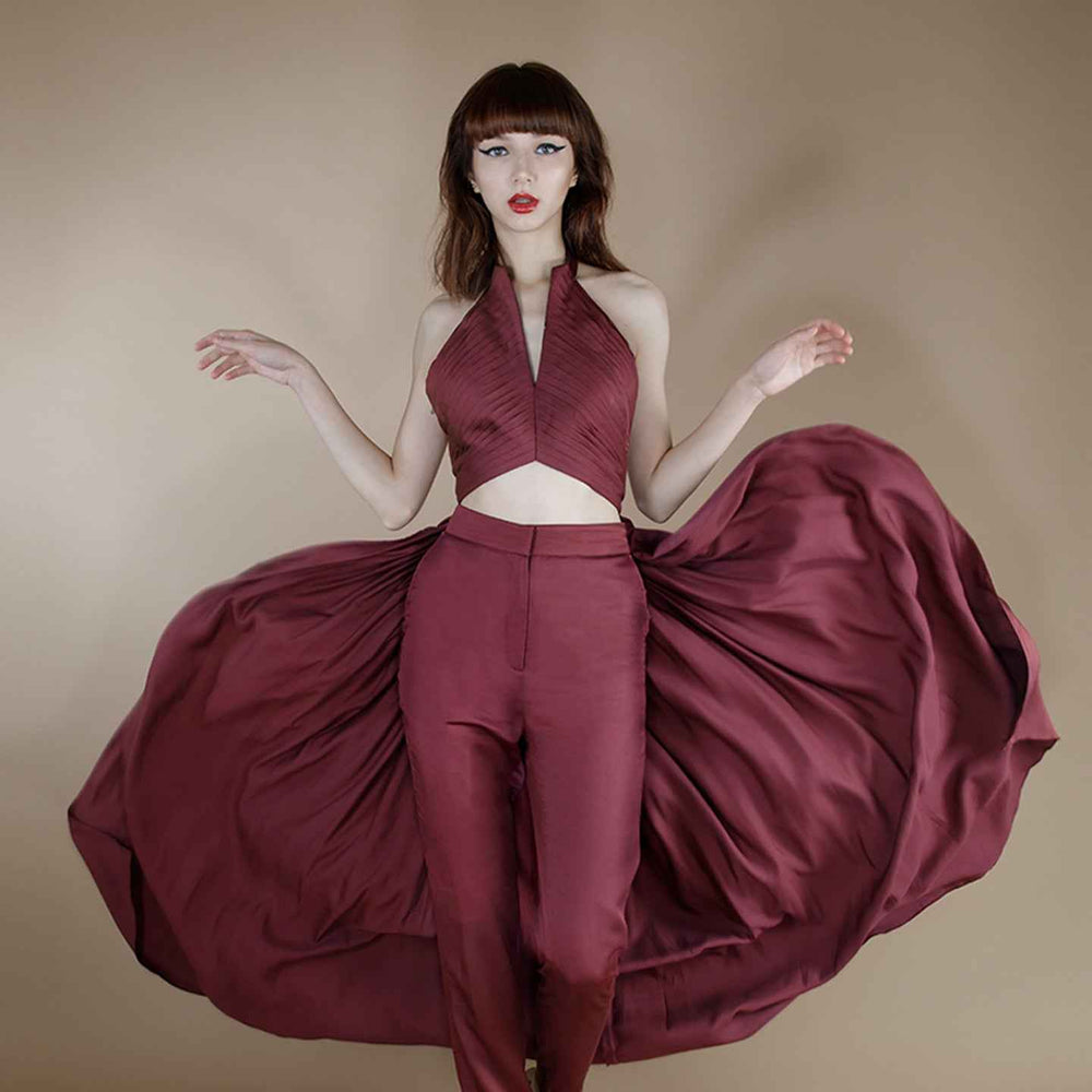 Front view of the maroon halter crop top with a voluminous pleated cape, styled with matching trousers