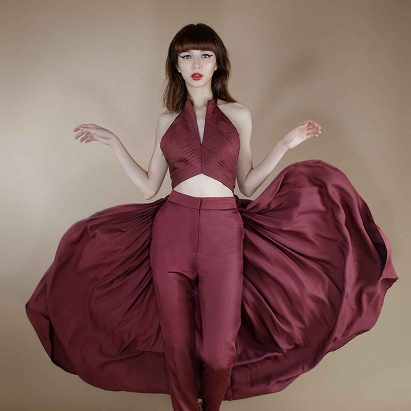 Front view of the maroon halter crop top with a voluminous pleated cape, styled with matching trousers