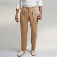 Close-up front view of the beige pleated trousers showing the waistband and pleat detail