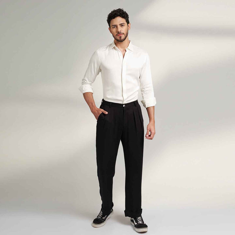 Front view of the black pleated trousers, full length with a white shirt