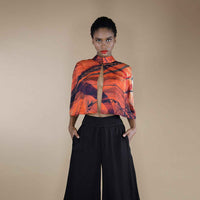Front view of the orange and black print cropped cape top styled with black wide-leg trousers