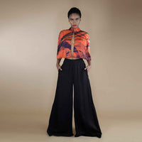 Angled front view of the orange and black print cape top and black wide-leg trousers
