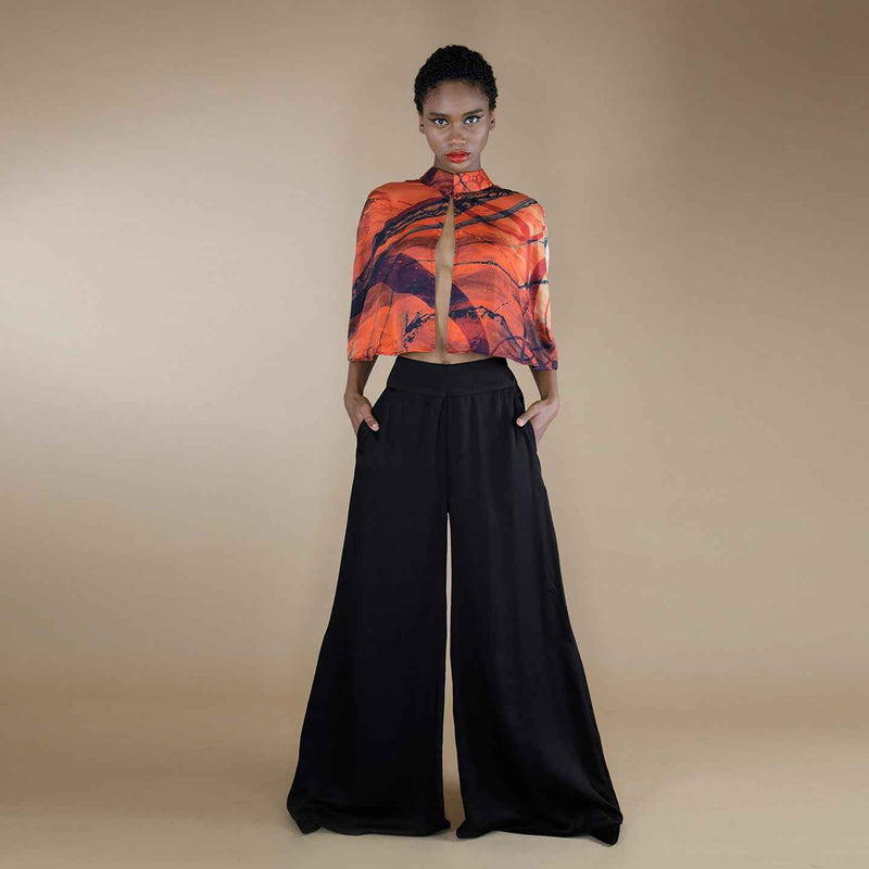 Front view of the black wide-leg palazzo trousers, styled with an orange print cape top