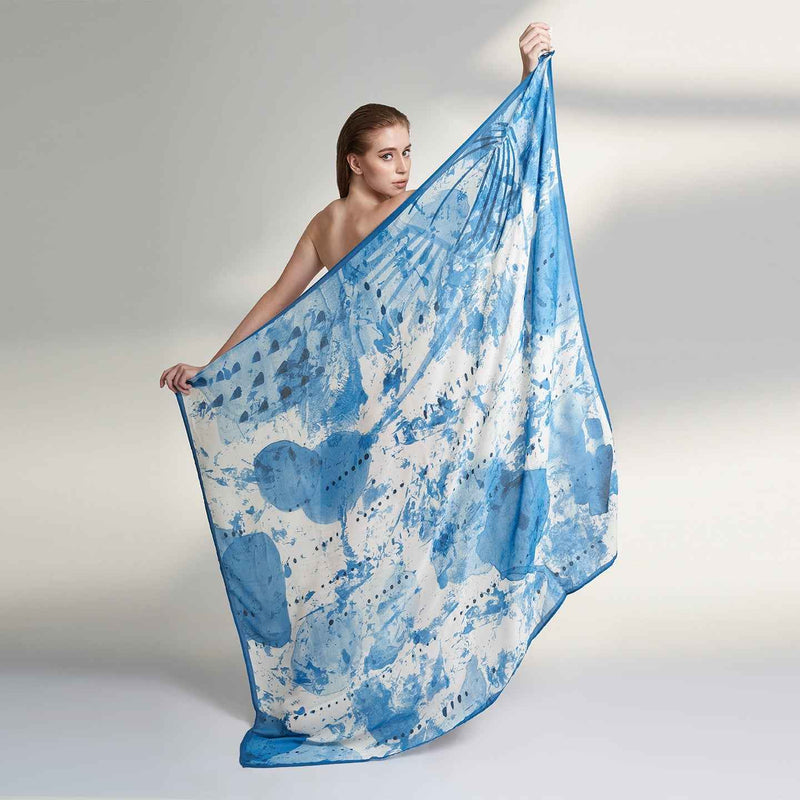Model holding out the blue and white watercolor splatter print scarf