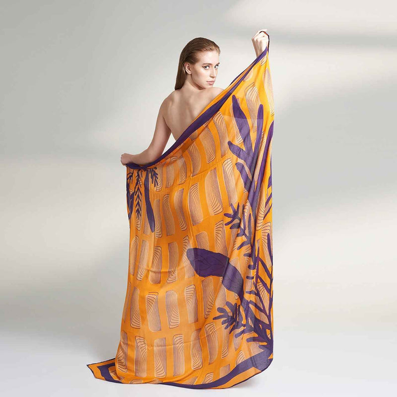 Front view of the model holding out the orange and purple leaf print scarf