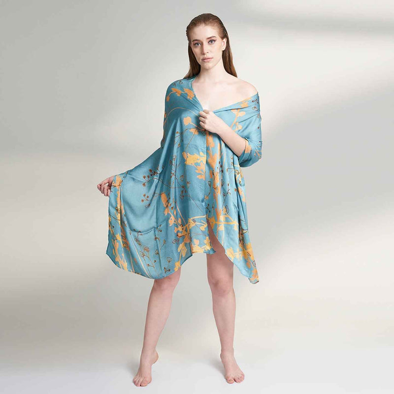 Model wearing the teal blue and gold branch print scarf as an off-shoulder wrap