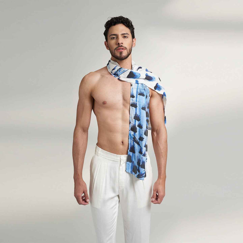 Front view of a man wearing the blue and navy paint-dab print scarf with white trousers