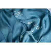 Close-up of the teal scarf fabric showing a small branch motif, gathered