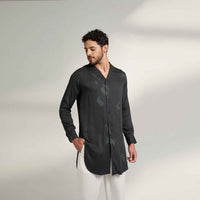 Angled front view of the longline black and grey tonal print shirt with a notch collar, styled with white trousers