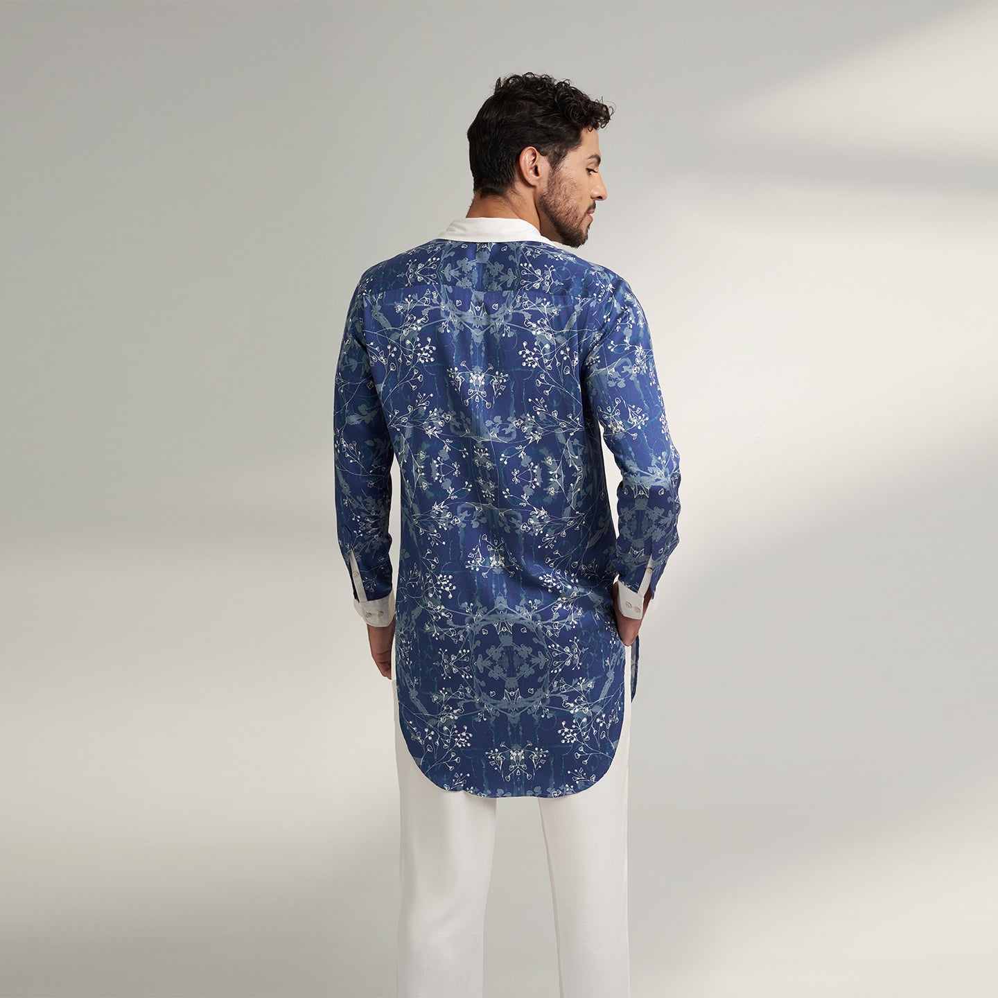 A long cuban collar shirt printed in blue and white made from organic lotus stem fabric white solid cuff and collar in white. the shirt has a comfort fit and it falls at mid thing
