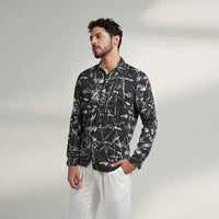 Angled front view of the black and white leafy print shirt styled with white trousers