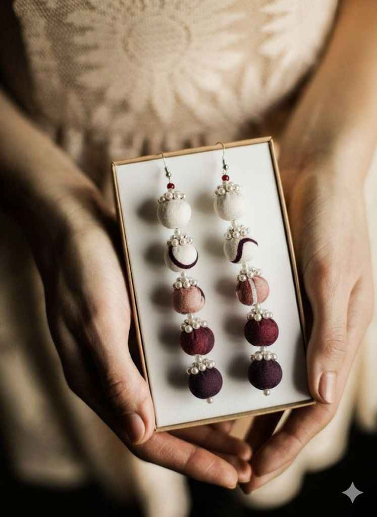 Close-up of hands holding a gift box with ombre maroon beaded drop earrings featuring pearl accents