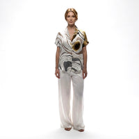 Front view of the abstract brown, grey and gold print shirt styled with white wide-leg trousers